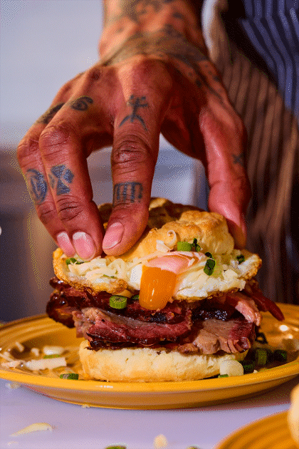 A tattooed chef hand puts the top on an egg and austin blues beef brisket sandwich