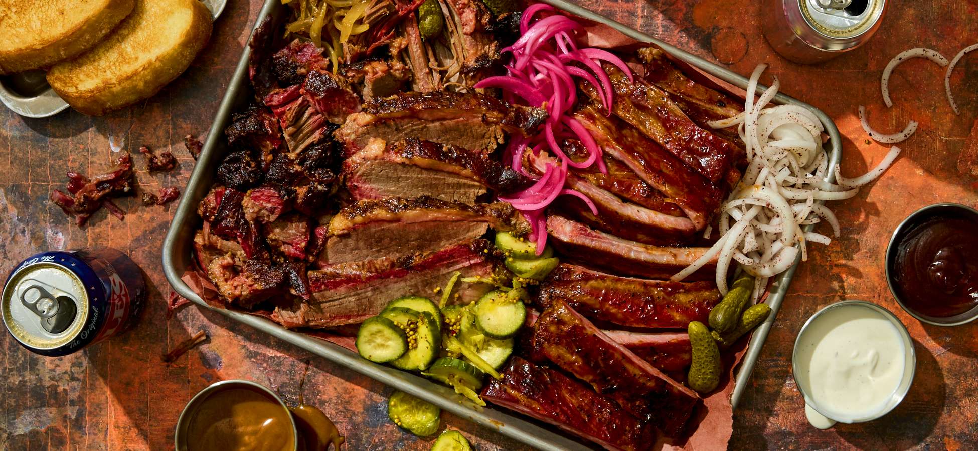 Overhead shot of a deliciously packed tray of Austin Blues smoked meats and barbecue on a table with other condiments and drinks